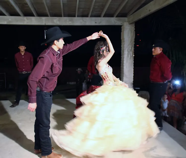 A dancer in western wear partnering a girl in a full yellow quinceañera gown
